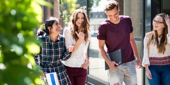 Vier Studierende unterhalten sich auf einer Straße vor einem Gebäude