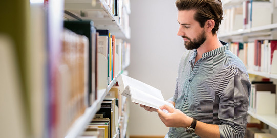 Ein Studi liest ein Buch in der Bibliothek