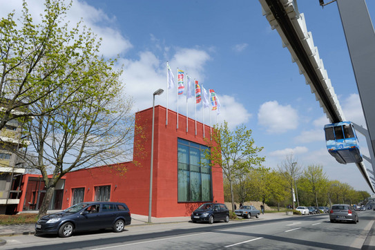 IBZ building surrounded by trees against blue sky. H-Bahn on the right.